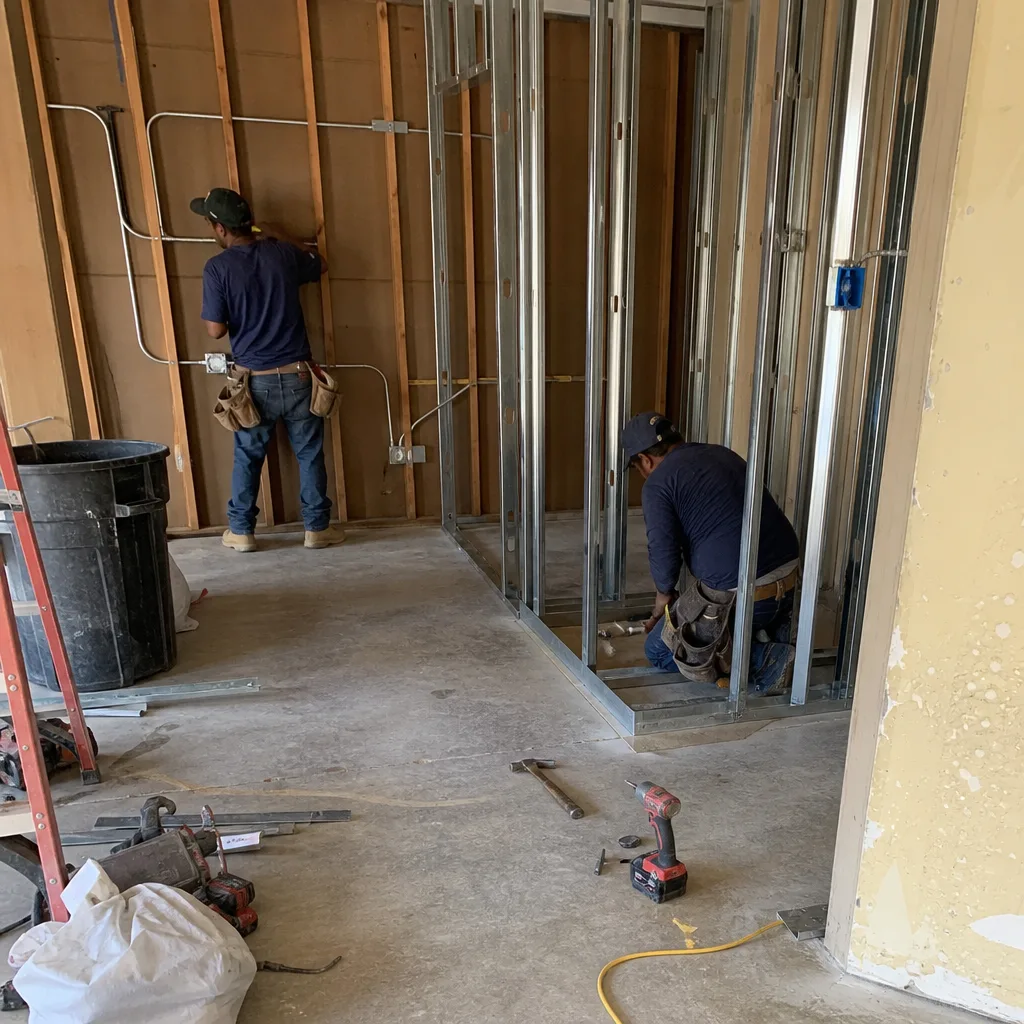 Two construction workers installing metal wall framing for garage conversion.